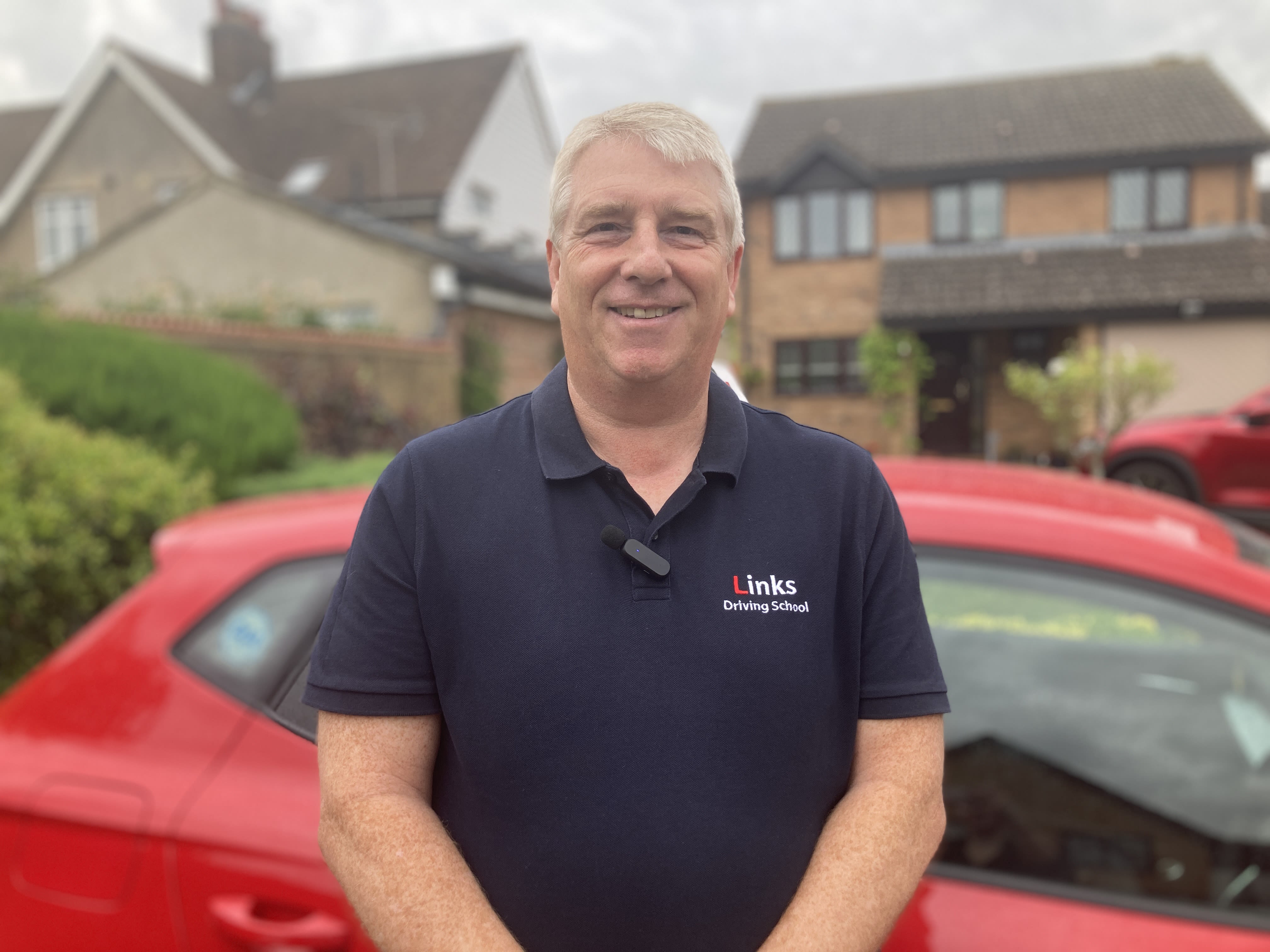 Neil Emmerson, a driving instructor stood infront of his red learner car